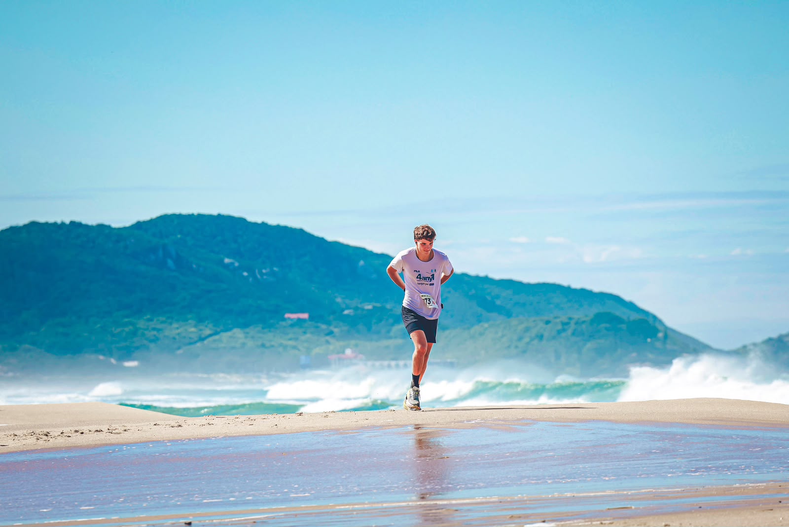 Atleta correndo na praia com ondas ao fundo